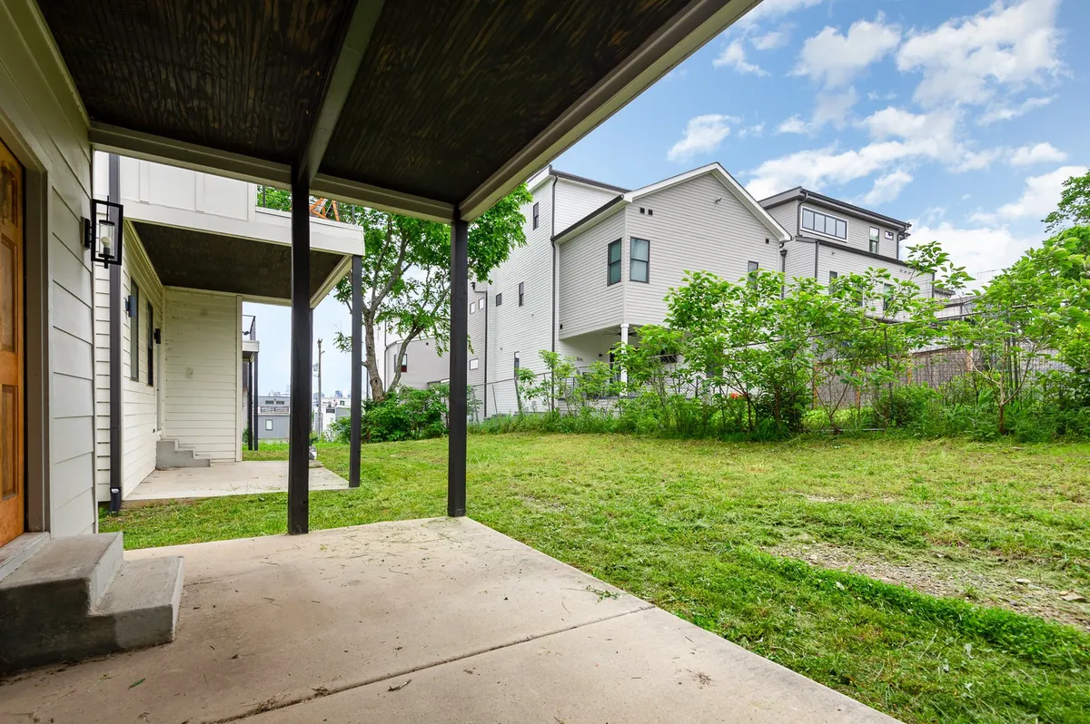 A charming private patio just outside the living area, surrounded by lush greenery and adjacent homes. The space features outdoor seating, perfect for morning coffee or evening relaxation, and seamlessly extends the indoor gathering area outdoors.