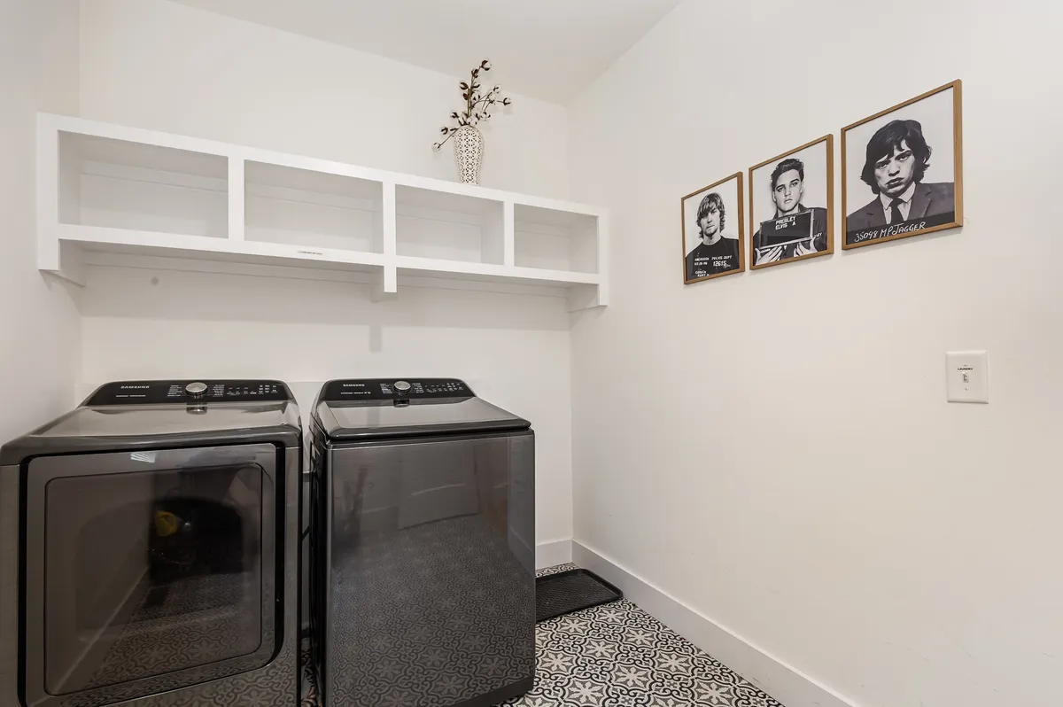 A contemporary laundry room featuring a sleek washer and dryer, stylish decorative elements such as a vase and framed photographs, and a sense of organization and cleanliness.