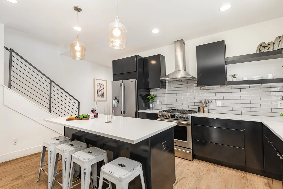 A view of a stylish island countertop paired with stainless steel appliances, open shelving, and pendant lighting, creating a contemporary and sociable kitchen setting. The space suggests easy movement between cooking and entertaining.