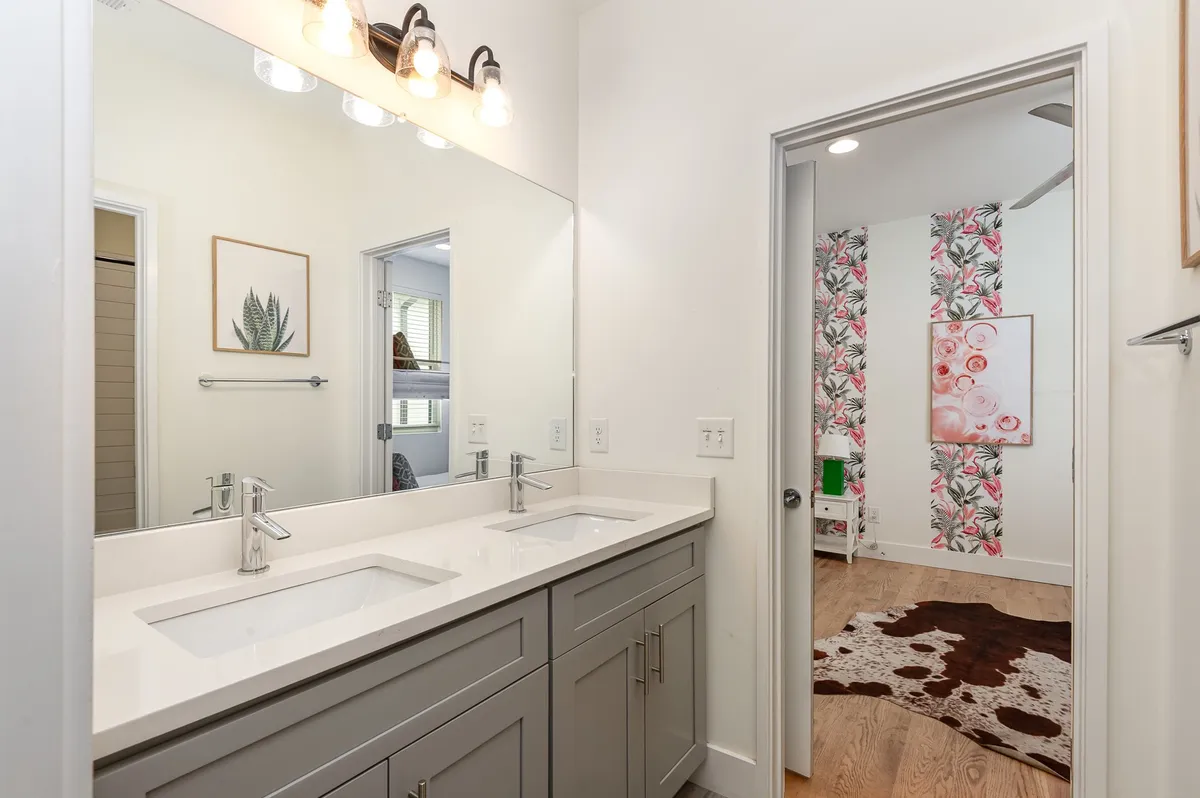 A bright, fresh bathroom with double vanities, a large mirror, and floral wallpaper. The space is designed for shared use during busy mornings, with ample lighting and modern fixtures.