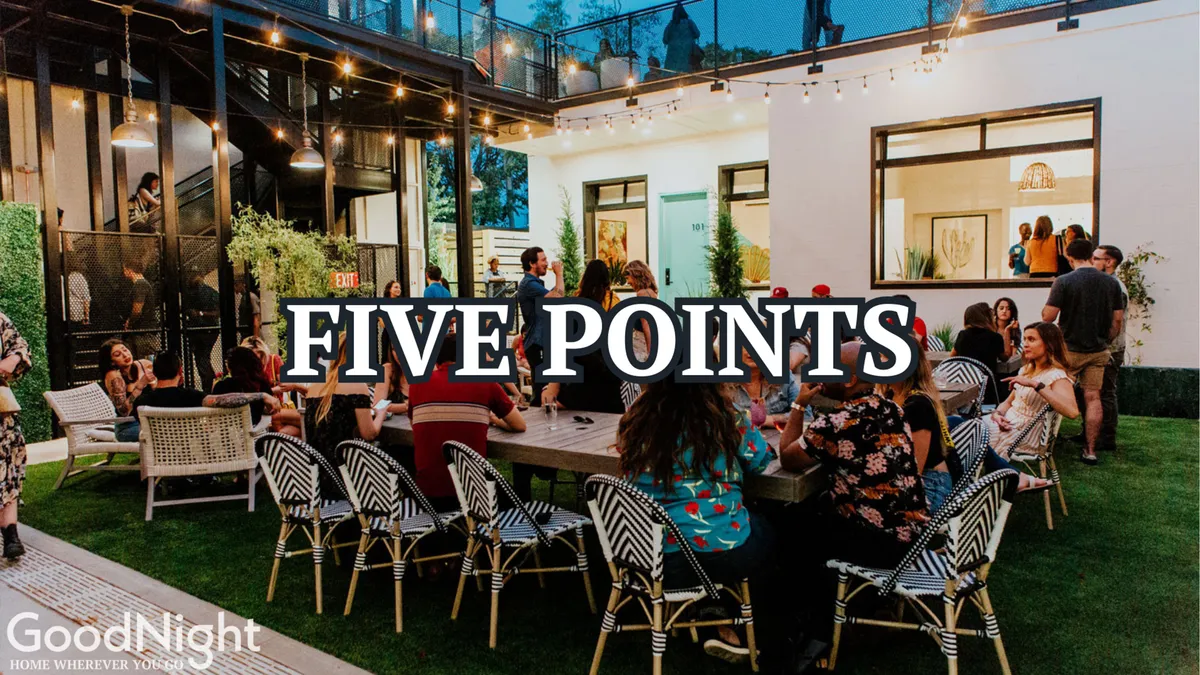 A vibrant outdoor dining area filled with people socializing under string lights, set against the backdrop of modern architecture and a neatly kept lawn. The scene conveys a sense of camaraderie, relaxation, and opportunities for informal gatherings outside of meetings.