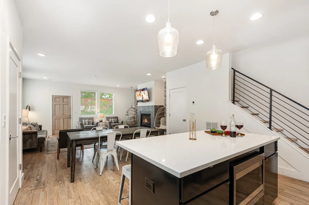 A bright, open-concept living space featuring a kitchen island, dining table, spacious living area with a stylish sofa, a modern fireplace, and a large television. The room’s layout encourages easy movement and interaction, while contemporary decor and ample lighting make the space inviting.