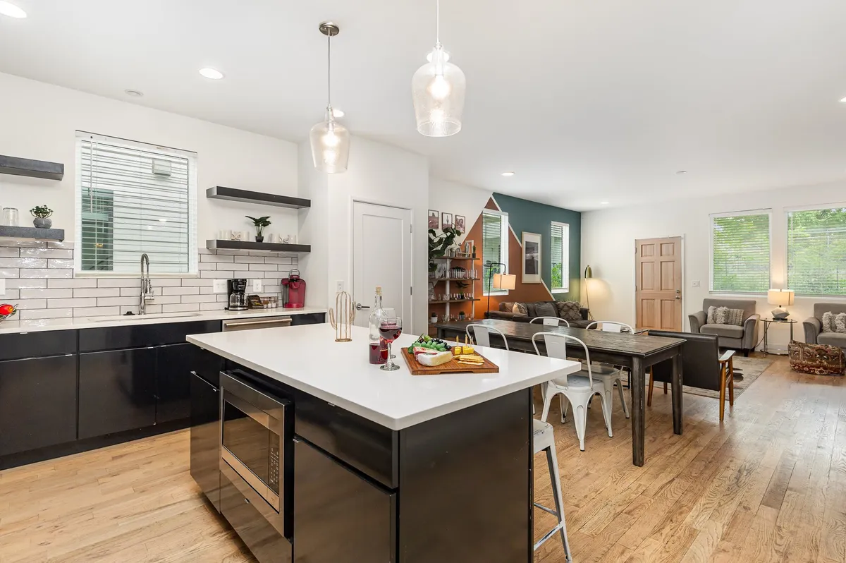A bright, airy kitchen and dining space with a kitchen island, dining table for four, and open shelves adorned with plants. The layout seamlessly connects the cooking area with the dining area, creating an ideal environment for group meals and conversation.